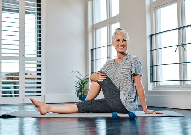 One should always stretch before attempting to do yoga. Portrait of a cheerful mature woman practicing yoga inside of a studio during the day - Fotografie, Obrázek