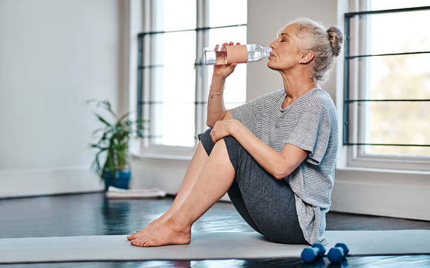 Пей до дна. зрелая женщина, практикующая йогу, выпивая воду в студии в течение дня - Фото, изображение