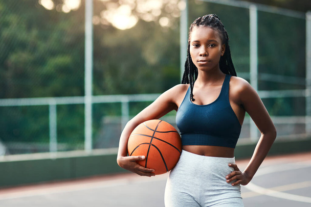 Νιώθω σαν στο σπίτι μου στο γήπεδο. μια ελκυστική νεαρή αθλήτρια που στέκεται στο γήπεδο μόνη της και κρατά μια μπάλα μπάσκετ κατά τη διάρκεια της ημέρας - Φωτογραφία, εικόνα