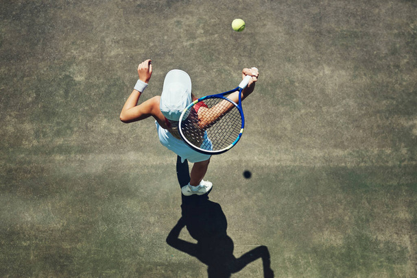 Επιστρέφω σε σένα. Στιγμιότυπο υψηλής γωνίας μιας συγκεντρωμένης νεαρής γυναίκας που παίζει τένις έξω σε γήπεδο τένις κατά τη διάρκεια της ημέρας - Φωτογραφία, εικόνα
