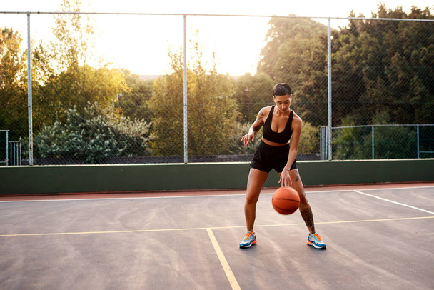 Getting into the swing of things. Full length shot of an attractive young sportswoman standing alone on a basketball court and warming up with the ball - Fotografie, Obrázek