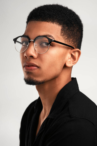 He has his eye on you. Portrait of a handsome young man wearing glasses while standing against a grey background inside of a studio - Foto, imagen