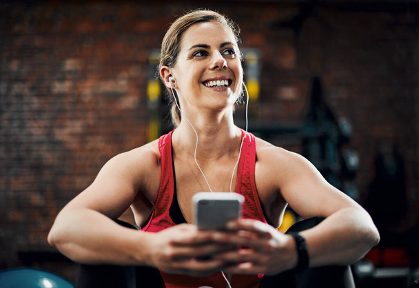 The perfect workout track. an attractive young female listening to music while working out in the gym - Foto, afbeelding
