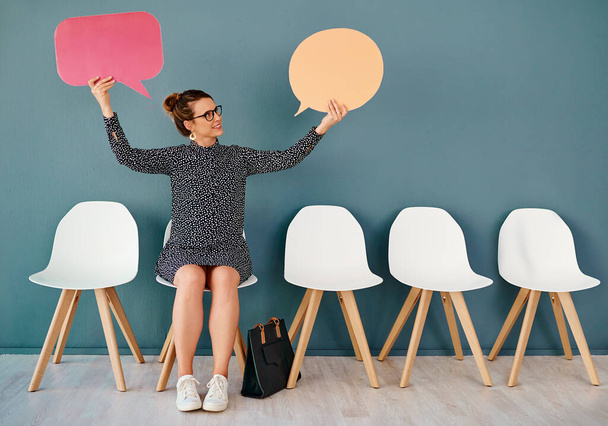 Is that so. Studio shot of an attractive young businesswoman holding up speech bubbles while sitting in line against a grey background - Zdjęcie, obraz