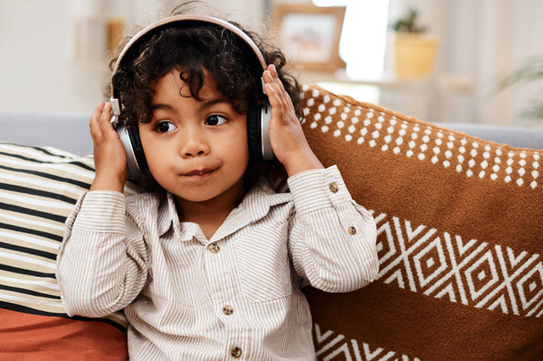 Я знаю хорошу пісню, коли чую її. чарівний маленький хлопчик слухає музику на навушниках, сидячи на дивані вдома
 - Фото, зображення