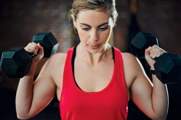 Пришло время заставить эти мышцы работать. привлекательная молодая спортсменка тренируется с гантелями в тренажерном зале - Фото, изображение