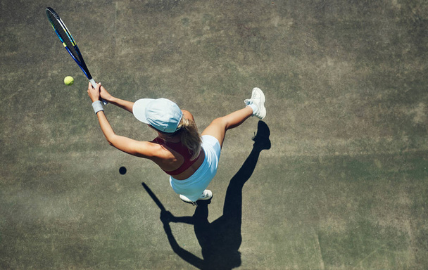 Keep swinging. High angle shot of a focused young woman playing tennis outside on a tennis court during the day - Foto, Imagen