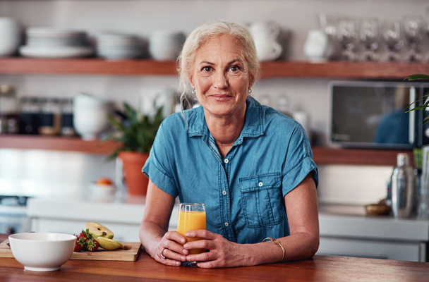 Τώρα αυτό είναι το πώς να ξεκινήσει μια μέρα. Καλλιεργημένο πορτρέτο μιας ελκυστικής ηλικιωμένης γυναίκας που απολαμβάνει ένα ποτήρι χυμό πορτοκαλιού ενώ ετοιμάζει πρωινό στην κουζίνα - Φωτογραφία, εικόνα