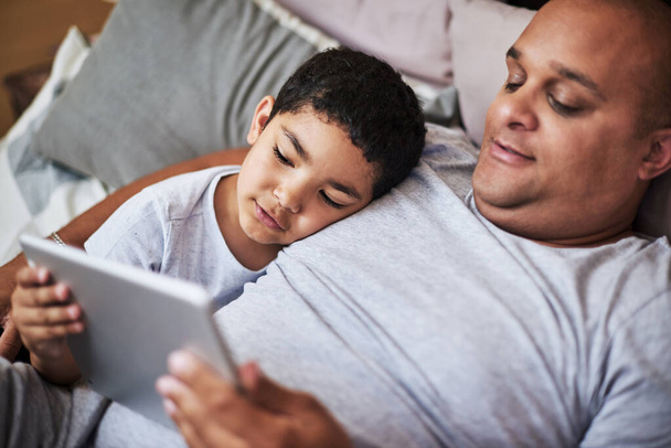 Dont fall asleep. a cheerful young man and his son watching videos on a digital tablet together while hanging out on a bed at home during the day - Zdjęcie, obraz