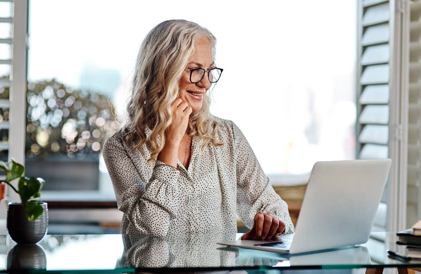Everythings turning out lovely after all. an attractive senior businesswoman looking thoughtful while working on a laptop at home - Фото, изображение
