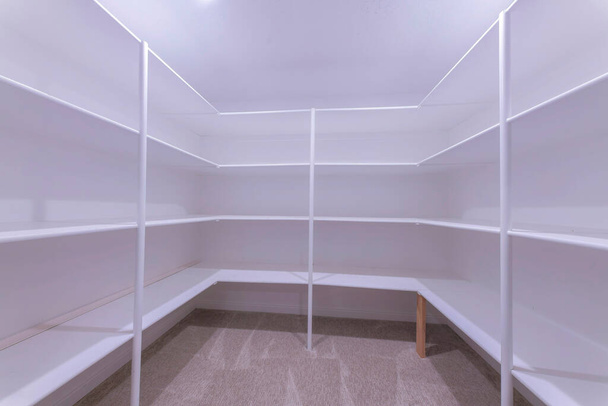 Kitchen pantry with white interior and carpeted flooring. Interior of a pantry with framed shelves on three parts of the wall and stand on the carpet floor. - Photo, image