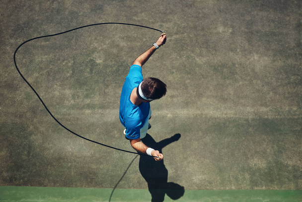 Λίγο ζέσταμα μόνο. Υψηλής γωνίας βολή ενός εστιασμένου νεαρού άνδρα χρησιμοποιώντας ένα σχοινάκι σαν άσκηση έξω σε ένα γήπεδο τένις κατά τη διάρκεια της ημέρας - Φωτογραφία, εικόνα