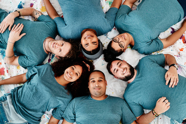 Taking a break. High angle portrait of a diverse group of friends lying down in a circle during an art class - Fotó, kép