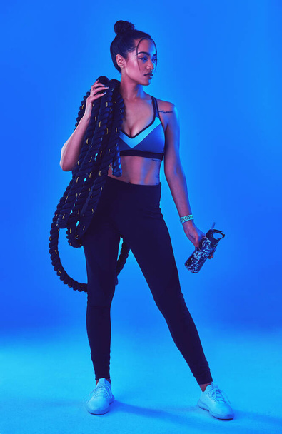 Shes always ready for a challenge. Full length shot of an attractive young sportswoman posing carrying battle ropes against a blue background - Photo, Image