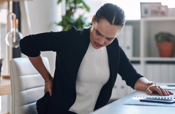 Ive been sitting here for way too long. an attractive young businesswoman suffering from back pain while working inside her office - Foto, immagini