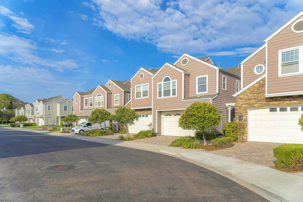 Townhouses with attached garage at Carlsbad, San Diego, California. There is an asphalt road pavement on the left and townhouses with pink and green exterior on the right. - Photo, image