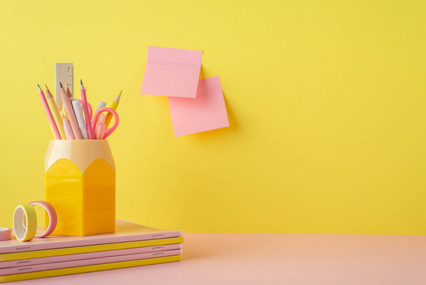 School supplies concept. Photo of trendy stationery on pink table stand for pens stack of copybooks adhesive tape and sticky note paper attached to yellow wall with copyspace - Foto, Imagen