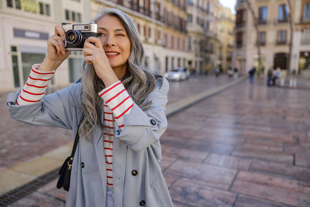 Koncentrált ázsiai nő elegáns ruhát tartja kamera a kezében, és fényképezés város látnivalók - Fotó, kép