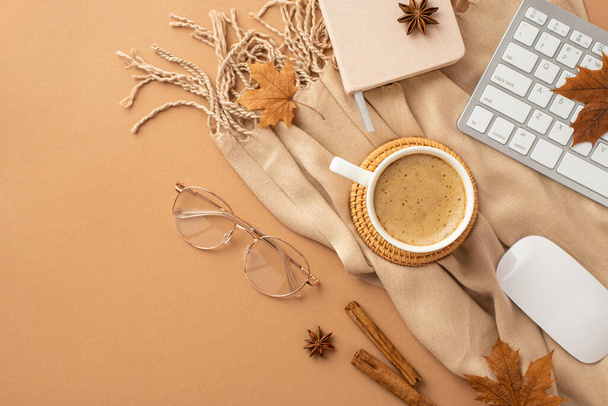 Autumn business concept. Top view photo of cup of frothy coffee rattan placemat planner computer mouse keyboard cinnamon sticks anise yellow maple leaves glasses and scarf on isolated beige background - Foto, Imagen