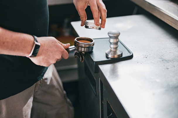 Barista holding tamper and press ground coffee in holder to make espresso for client in cafe - Foto, immagini