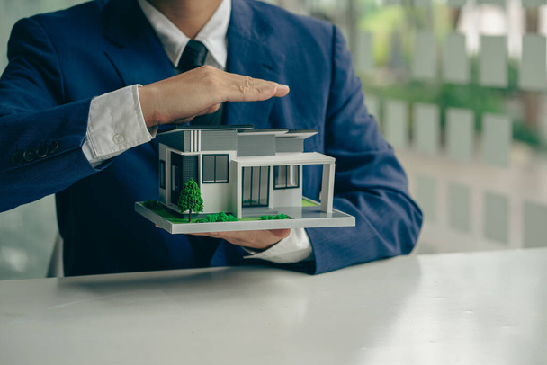 Hand-protected wooden toy house Businessman and wooden house model Real estate, insurance and property concepts - Foto, Imagen