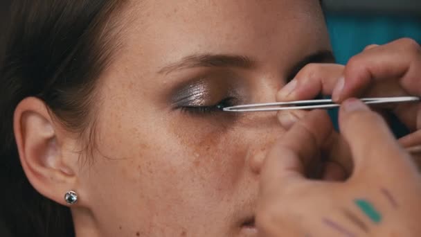Beautiful girl is put on make-up on her face and glues her eyelashes. Make-up artist paints a young womans face. Womens beauty. Emphasize the natural beauty of the girl. - Video