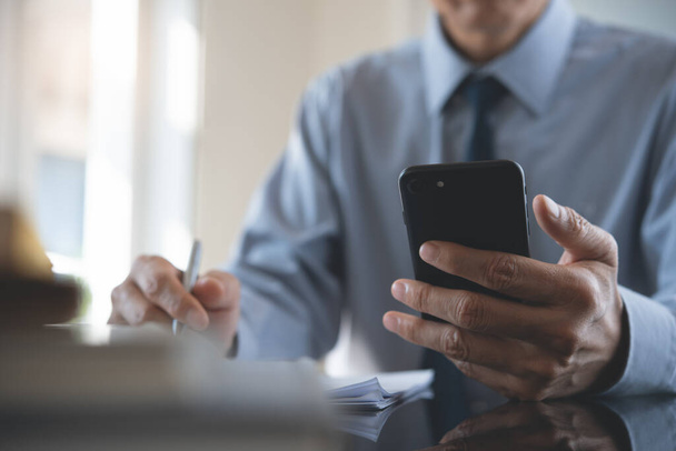 Phone connecting to colleagues, teamwork concept. Businessman using mobile smart phone while working in modern office with official business document on desk, close up. - Photo, image