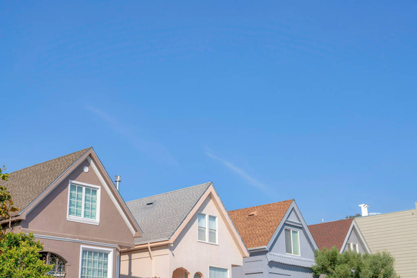 Side view of houses in a row with gable roofs at the suburbs of San Francisco, California. Small houses exterior with shingles on the roof against the clear blue sky. - Foto, afbeelding