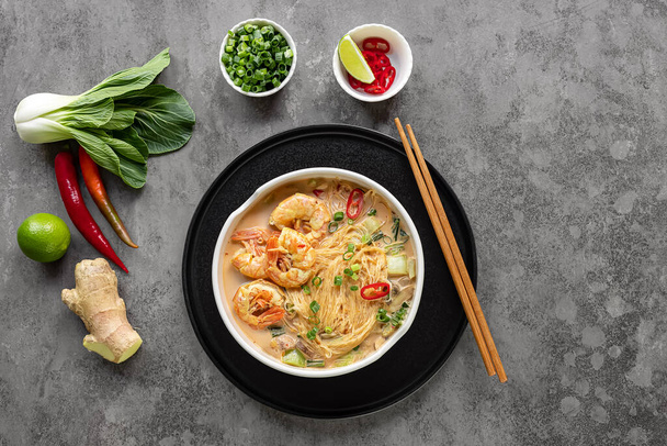 Laksa Shrimp bowl. glass noodle dish, top view, copy space. Asian Malaysian food with shrimps, bok choy, lime, ginger, and chili. Most variations of laksa are prepared with spicy coconut soup. - Zdjęcie, obraz