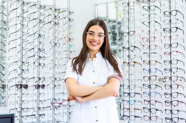 Optician selling glasses at the optics. Happy optician selling glasses and looking at the camera smiling. Friendly eye doctor selling glasses at an optician's shop and looking at the camera smiling - Foto, imagen
