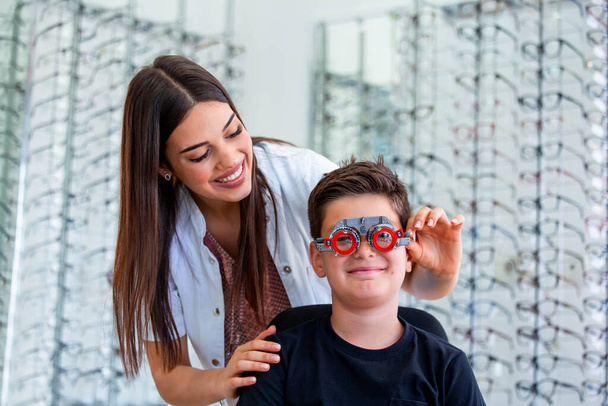 Vonzó szemész vizsgálata youg fiú optometrista tárgyalás keretben. Gyerek beteg, hogy ellenőrizze látás szemészeti klinikán. - Fotó, kép