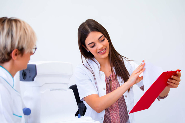oftalmologo femminile che mostra i dati del paziente in un blocco appunti, lavorando in un negozio ottico. Concetto di sanità e medicina
. - Foto, immagini