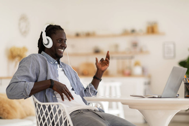 Cheerful Black Guy Wearing Headphones Playing Virtual Guitar While Listening Music On Laptop, Positive African American Man Having Fun While Working Remotely From Home Office, Copy Space - 写真・画像