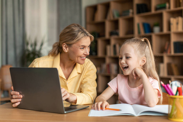 Online education. Happy mom and her little daughter using laptop, mother helping female child with homework and remote study, enjoying distance learning - Zdjęcie, obraz