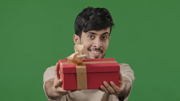 Латиноамериканец счастливый человек дарит подарок большой красный ящик с золотой лентой студии зеленый фон портрет дружественный индийский парень показывая подарок улыбающийся араб позволить приятный сюрприз юбилей концепции - Кадры, видео