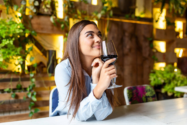 Beautiful woman tasting wine while sitting in restaurant. Image of cute pretty young woman sitting in cafe holding glass and drinking wine. portrait of a beautiful wine tasting tourist woman. - Fotografie, Obrázek