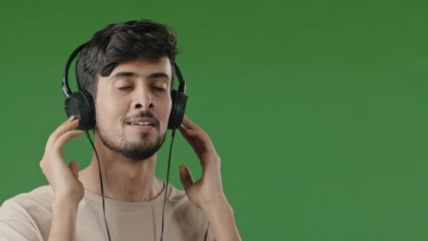 Крупный план счастливый веселый арабский человек слушать музыку использовать наушники наслаждаясь песня аудио любимая приятная мелодия беззаботный молодой латиноамериканец удовлетворил высокое качество звука танцы ритм на зеленом фоне - Кадры, видео