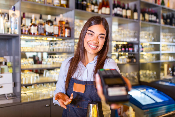 Waitress at cash counter holding an electronic card payment machine. Close up of young woman holding wireless terminal POS at coffee shop - Fotoğraf, Görsel