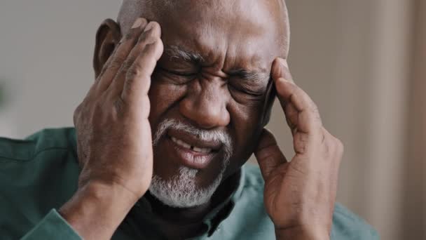 Close-up face sad elderly african american man feeling headache chronic migraine unhealthy multiracial grandpa massaging temples unhealthy middle aged 60s retired male suffering high blood pressure - 映像、動画