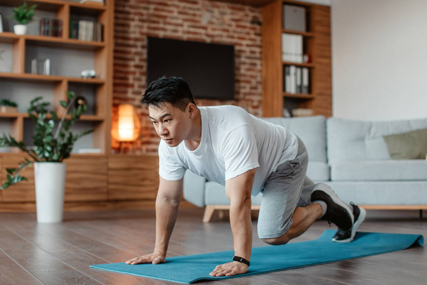 Sporty asian middle aged man doing running plank exercise, training on yoga mat at home in living room, copy space. Male fitness workout and sport motivation concept - Fotó, kép
