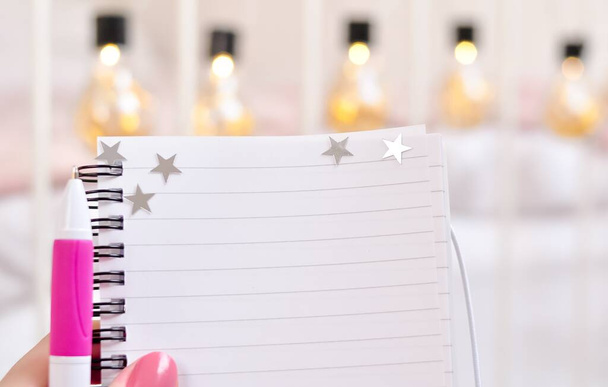 Notebook in hand with stars and pink pen for notes copy space. High quality photo - Zdjęcie, obraz