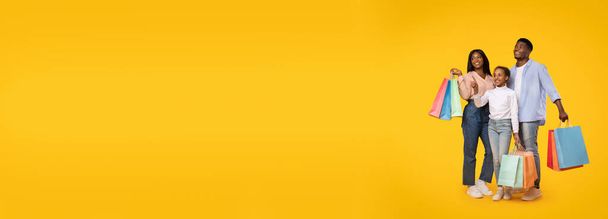 Чудова пропозиція за покупками. Африканська американська сім "я, яка носить сумки для покупців і дивиться убік на вільне місце над жовтим фоном, насолоджується сезонними продажами, панорамою з копіюванням. - Фото, зображення