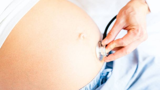 Orvosi konzultáció terhes nővel. Orvosi rendelő terhességi tanácsadónak. Az orvos megvizsgálja a terhes nőt, aki sztetoszkópot tart a hasában. Fogantatás anyaság, terhesség, szülés - Fotó, kép