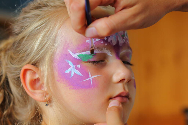 Children's face painting. The artist paints a princess crown on a small white blonde girl. - Photo, image