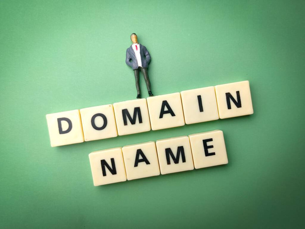 A miniature male figure on top of blocks with "DOMAIN NAME" text against a green background - Fotografie, Obrázek