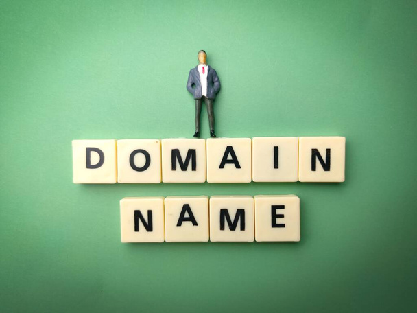 A miniature male figure on top of blocks with "DOMAIN NAME" text against a green background - Fotó, kép