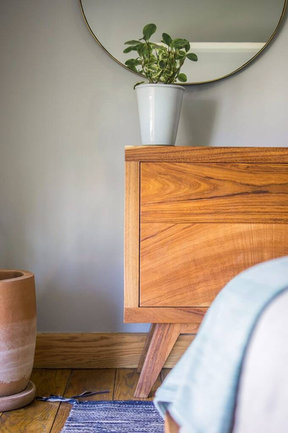 A wooden nightstand table with a plant at the top standing in the modernly furnished room - Foto, Imagem