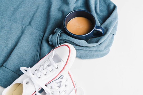 Nahaufnahme einer Tasse Kaffee mit Turnschuhen und blauem Hemd - Foto, Bild