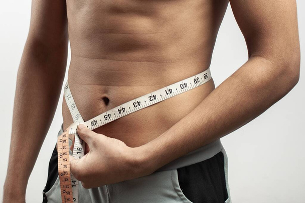 fitness model measuring his waist size with tape measure isolated on white background - Fotoğraf, Görsel