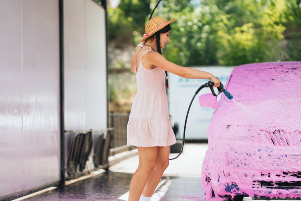 Brünette mit langen Haaren aus einem Hochdruckschlauch trägt in einer Waschanlage einen Reiniger auf das Auto auf - Foto, Bild